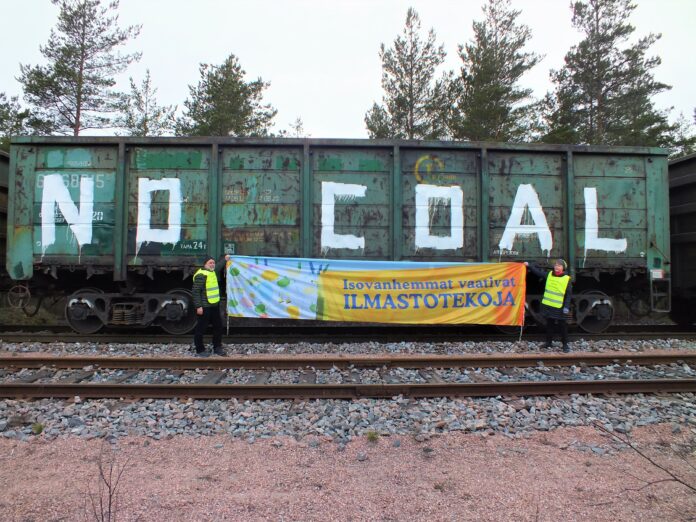 Ilmastoisovanhempien baderolli pysäytetyn hiilijunan vieressä. Junan vaunussa teksti no coal